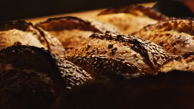 Loaves of bread sprinkled with sunflower pumpkin seeds lie on wooden rack. Fresh wholemeal loaves gradually cool after emerging from oven