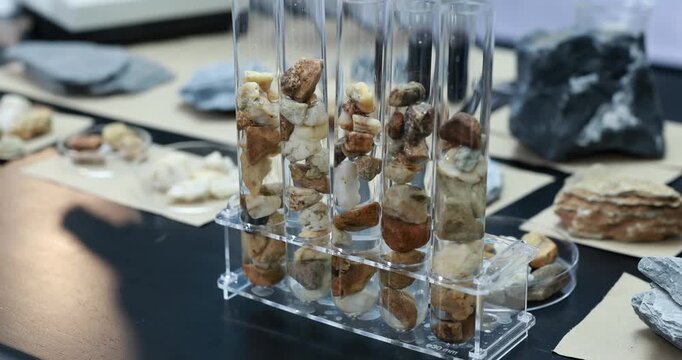 Clear glass tubes filled with layered white and brown rock samples on a display stand, with mineral specimens arranged on a table in the background.