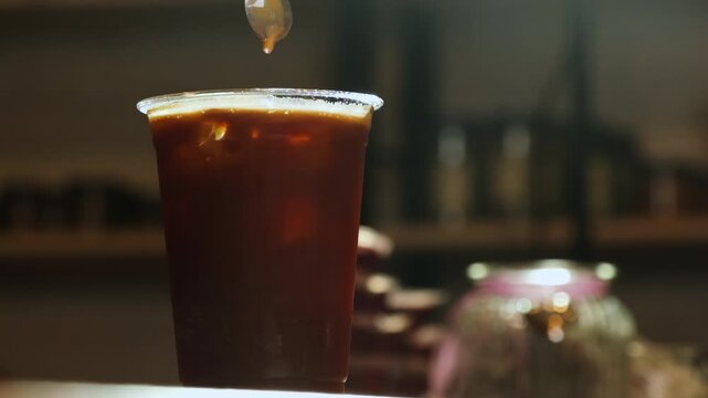 Tasty cold coffee cocktail with ice cubes and soda stirring in cafe closeup. Offering refreshing summer drink in plastic cup in coffeeshop