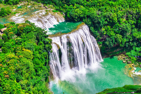 Aerial view captures cascading streams of Huangguoshu Waterfall plunging into a turquoise pool amidst lush green forest in Guizhou, China.