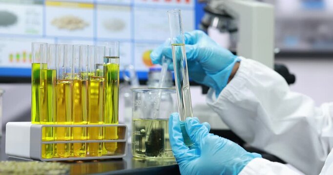 Scientist in blue gloves handles test tubes with yellow liquid in a modern laboratory, with a microscope and research samples in the background.
