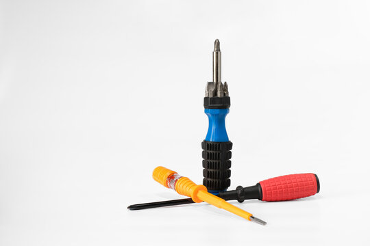 A multi-bit screwdriver standing upright among two crossed screwdrivers with red and orange handles, isolated on a white background.