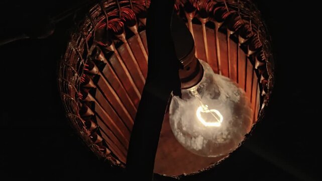 Glowing tungsten bulb hanging inside an old copper stator coil of an electric motor, representing industrial recycling, manual repair work, and the bright spark of technical innovation.