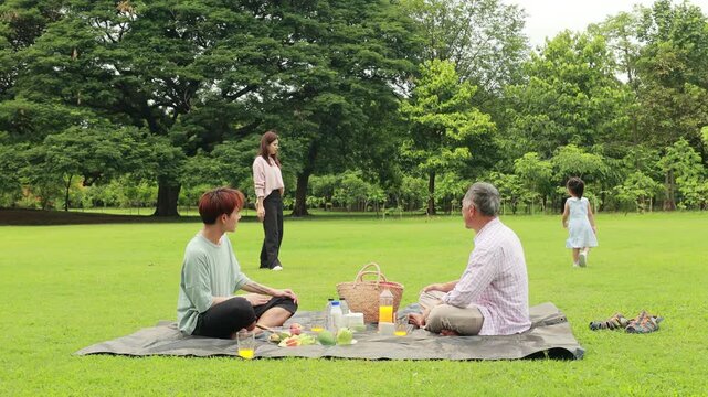 child runs with mother in summer field, small child playing on the lawn. spending time with father in the park. Happy Asian family having fun time on picnic at city nature park, outdoor activitie