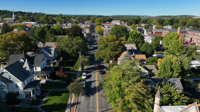 Backwards aerial reveal of car driving on small town America street. Large green trees in old, historic town with churches, Nazareth, Pennsylvania.