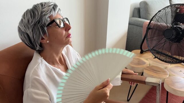 Mujer con sofocos de menopausia abanic&aacute;ndose con ventilador