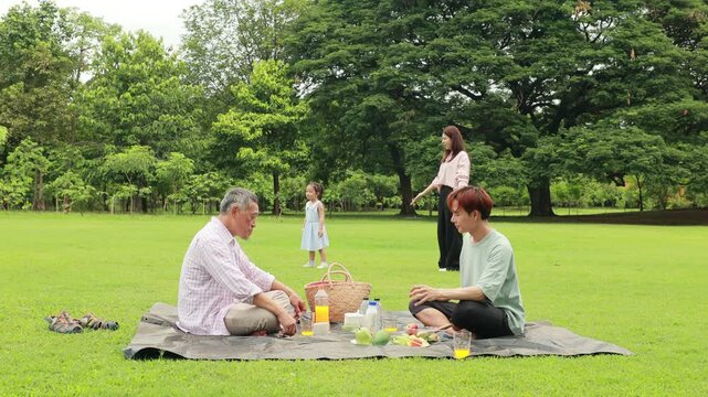 child runs with mother in summer field, small child playing on the lawn. spending time with father in the park. Happy Asian family having fun time on picnic at city nature park, outdoor activitie