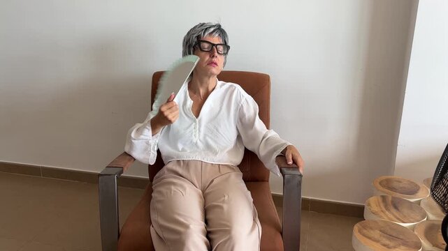 Mujer con sofocos de menopausia abanic&aacute;ndose en un sill&oacute;n