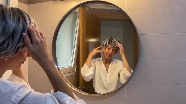 Mujer menop&aacute;usica pein&aacute;ndose sus canas frente al espejo