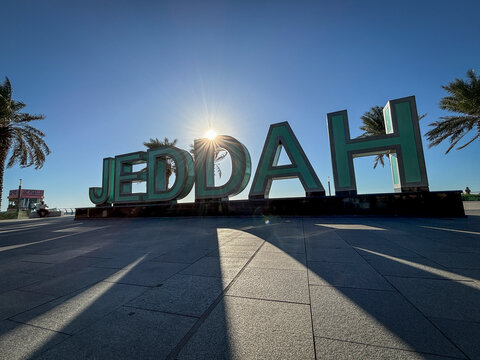 The sun shines between the letters of the Jeddah sign on the corniche at sunrise, Makkah, Jeddah, Saudi Arabia