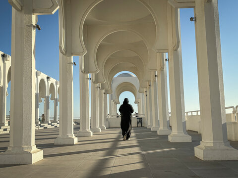 A woman walks alone through the colonnaded gallery toward the domed mosque, Makkah, Jeddah, Saudi Arabia
