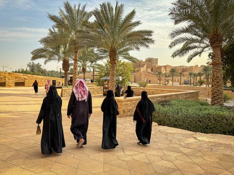 A group of women and a man walk a palm-lined path in Diriyah's historic district, Riyadh, Riyadh, Saudi Arabia