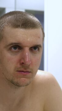 Shower routine continues as man presses wet hands over face and forehead. Bare chested man lowers his hands and stares ahead, showing calm, pensive expression in bathroom, with wet hair and skin.