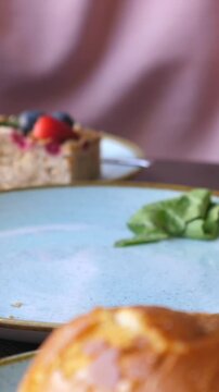 Close hand movement around burger bun suggests serving or finishing sandwich assembly on ceramic plate. Crisp lettuce, tomato and soft bun stand out in warm culinary close up during meal preparation.