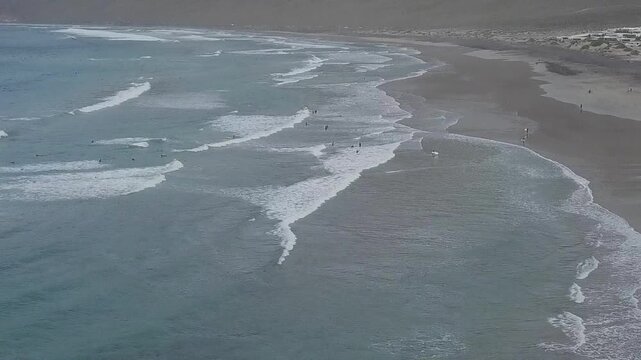 Waves along a beach beneath volcanic cliffs