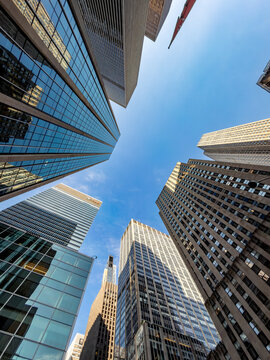 Low angle worm eye perspective of glass skyscraper facades against blue sky. High rise modern glass and steel office buildings pointing upward toward clear blue sky, low angle view.