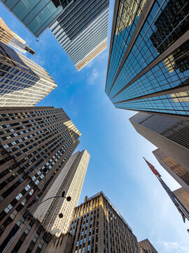 Upward perspective of glass office towers against blue sky. Worm eye view showing tall modern commercial skyscrapers surrounding a blue clear sky in Manhattan.
