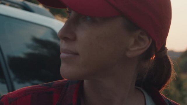 Young woman stands by the big 4x4 off road car and watches sunset in the wild