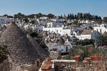 An elevated view over the historic Rioni Monti district showing corbelled trulli roofs amid whitewashed buildings and cypress trees, Alberobello, Puglia, Italy. © Adriano