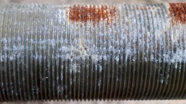 Panning shot of rusty fine screw threads on large mechanical steel shaft outdoor.