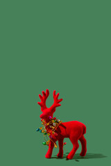 Red plush reindeer tangled in colorful holiday lights against a green background. Winter holiday design or Christmas decoration concept. © Maja 