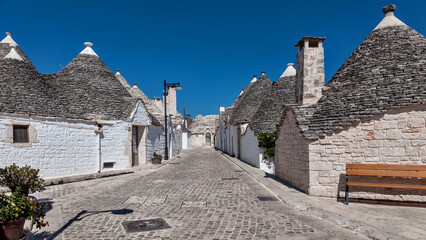 A paved street flanked by drystone trulli with conical corbelled roofs and whitewashed lower walls, Alberobello, Puglia, Italy. © Adriano