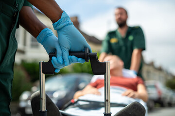 Paramedics assist a patient on a stretcher in an outdoor setting.
