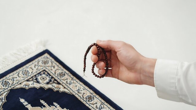 Muslim prayer beads are held gently near a traditional rug.