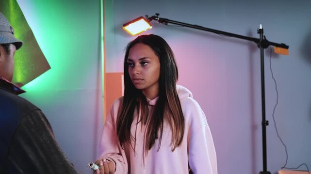 Three multiracial actors engage in a collaborative and comedic exchange inside a professional indoor studio with lighting and reflector equipment.