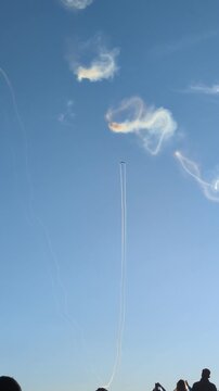 Spectacular aerobatics airshow performance with a stunt airplane flying high in a clear blue sky, leaving a white smoke trail and creating circular smoke rings during an outdoor summer aviation event.