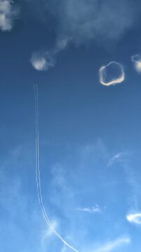 Spectacular aerobatics airshow performance with a stunt airplane flying high in a clear blue sky, leaving a white smoke trail and creating circular smoke rings during an outdoor summer aviation event.