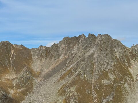 High-altitude panoramic mountain view in the Swiss Alps near Realp, Uri, showing jagged rocky peaks, dramatic ridges, alpine valleys and cloud layers under a deep blue sky in the wild landscape