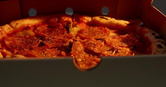 Close up shot of spicy salami pizza inside a delivery container. Warm golden light highlights the crispy charred crust and melted toppings.
