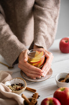 Hands holding warm apple cider, autumn lifestyle drink with apples