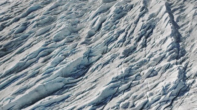Aerial flight over a frozen glacier with deep ice cracks and crevasses. Natural cold landscape background. 