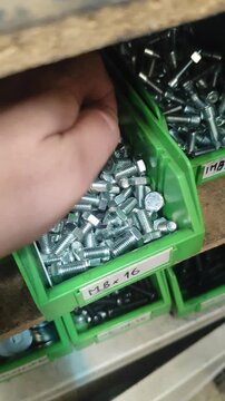 Hand Searching and Selecting Hex Bolts from Storage Bin in Workshop
