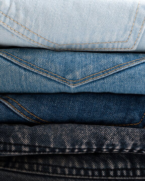 A close-up view of a neatly stacked pile of denim jeans in various shades of blue.