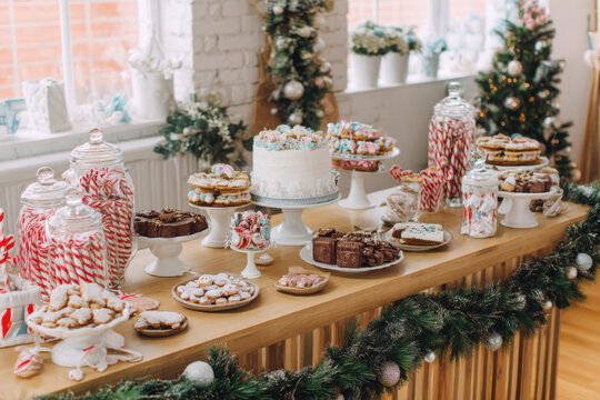 A festive christmas dessert table with sweet treats and cakes decorated with candy canes, cookies, and colorful sweets on a wooden table with green garland in a bright