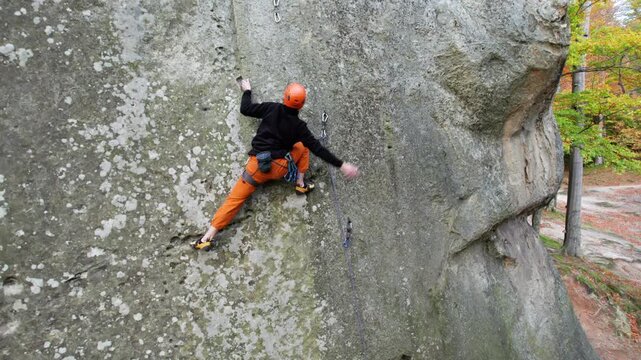 Aerial shot of male climber on massive stone wall framed by colorful woodland. Outdoor adventure footage for rock climbing, balance, courage, and active recreation branding