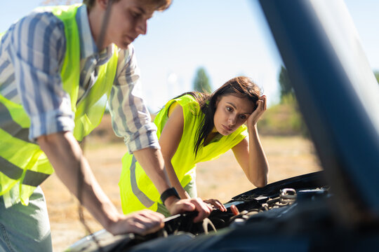 Frustrated couple checking broken car engine on roadside