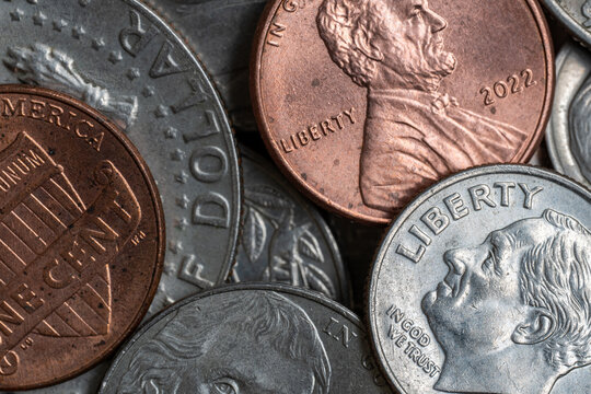 Detailed macro photograph of assorted United States coins including a Lincoln penny and Roosevelt dime, showing metallic surfaces, wear and engraved currency details.