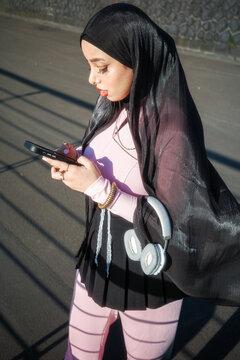 Woman in headscarf browsing phone on sunlit street