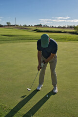 Obraz premium Senior golfer standing over the ball ready to putt, focused expression, green course stretching behind him.