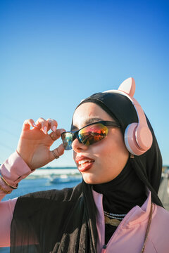 Woman with headphones adjusting shades by the water