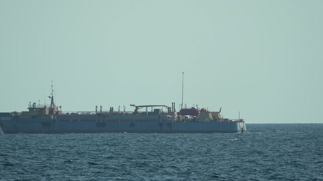 Dredge ship, sea, water A large industrial vessel navigating calm blue ocean under clear sky.