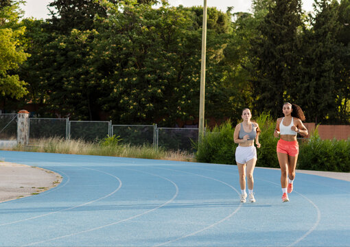 Young women running on blue athletic track