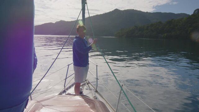 Young man enjoys the morning time on the sailing boat anchored in the calm bay