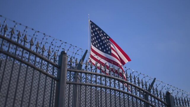 American flag behind metal gates and barbed wire, prison security concept