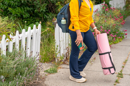 woman leaving house with yoga mat and phone backpack