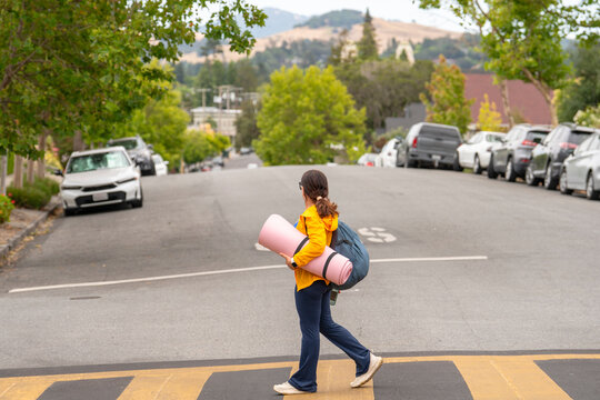 woman walking across crosswalk with yoga mat